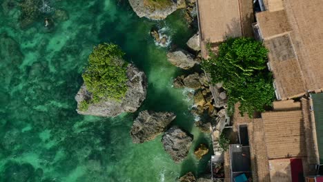 aerial top down view of cliffside homes on rocky coastline in uluwatu bali with turquoise ocean