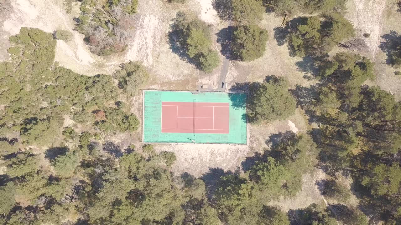 una vieja cancha de tenis en rojo y verde con muchos árboles alrededor