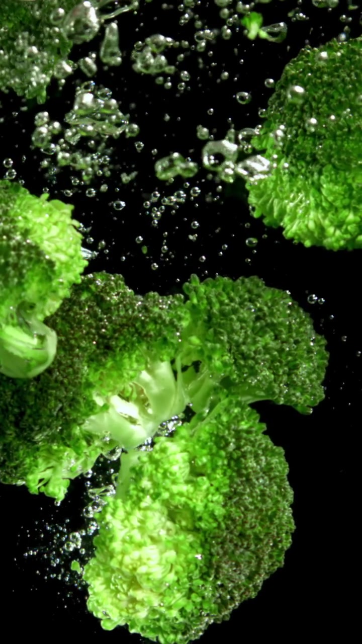 Cimette di broccoli verdi freschi che si immergono nell'acqua con bolle