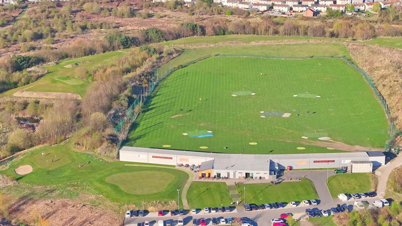 Wide aerial orbit of Waterfront Golf Club driving range in morning summer sunlight, Rotherham, South Yorkshire, UK