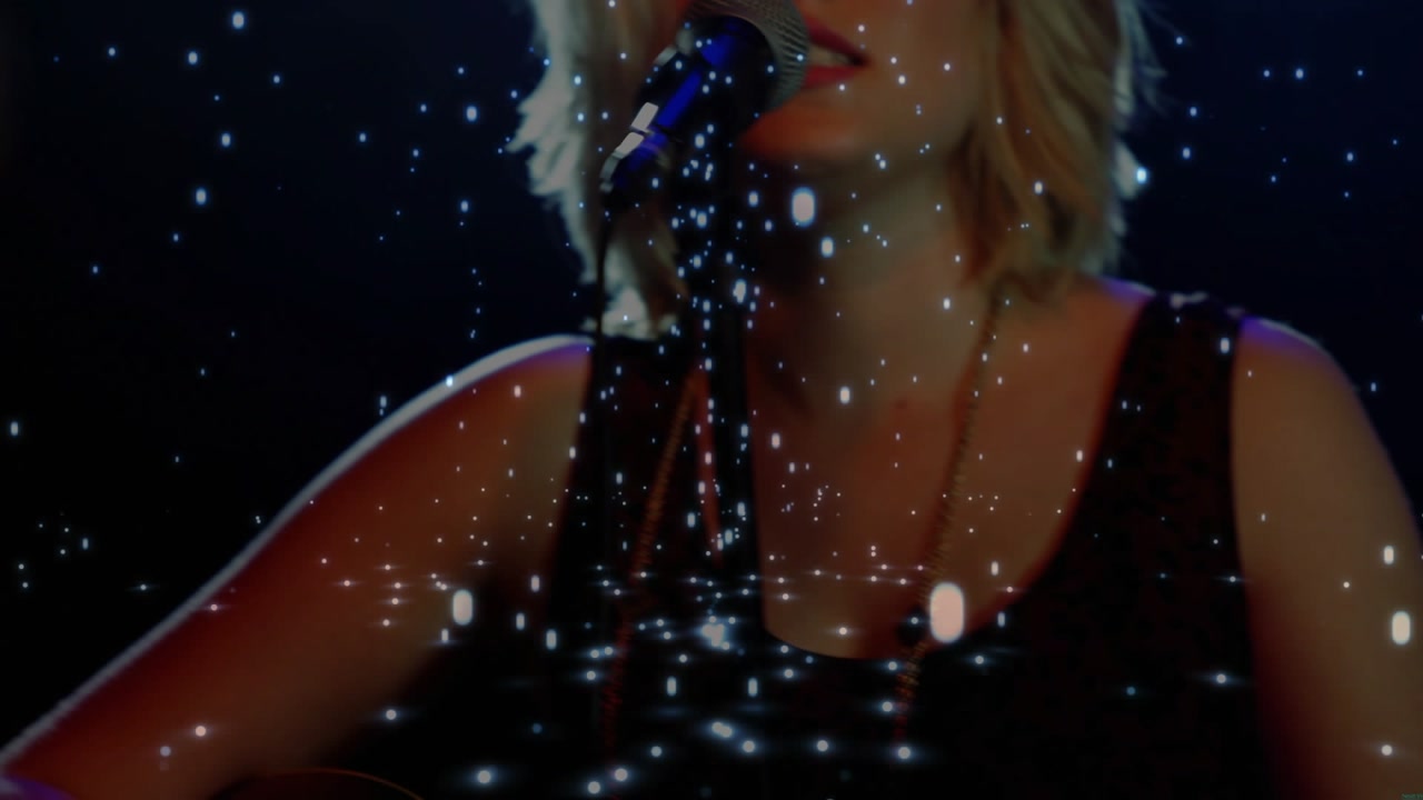 Woman musician adjusting left-hand on fret picking guitar and singing into mic under stars for song
