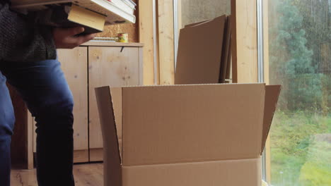 Man inside the room brings a stack of books in his arms and puts them in a cardboard box