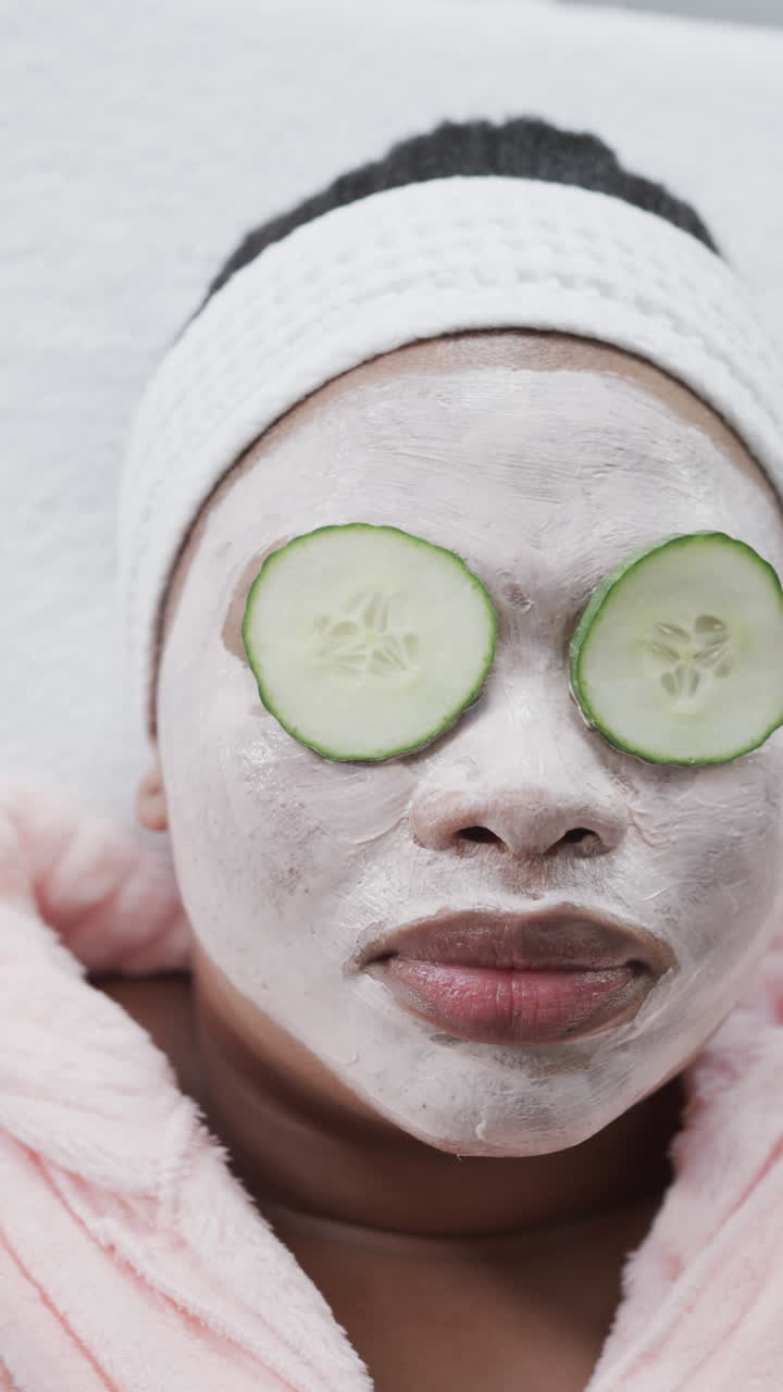 Vertical video close up of african american woman in beauty face mask with cucumber slices on eyes