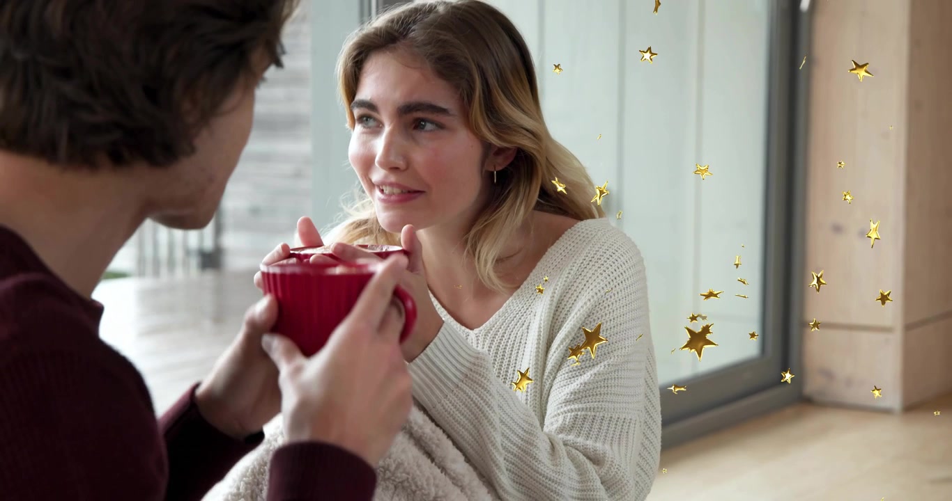 Marketing ad showing couple sharing warm moment offering red mugs on floor with drifting stars