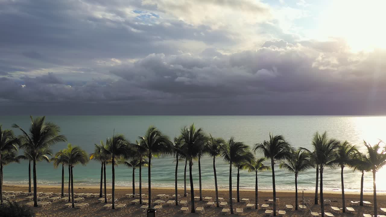 Aerial view of Cancun beach at sunrise over palm trees, calm waters, and dramatic clouds.