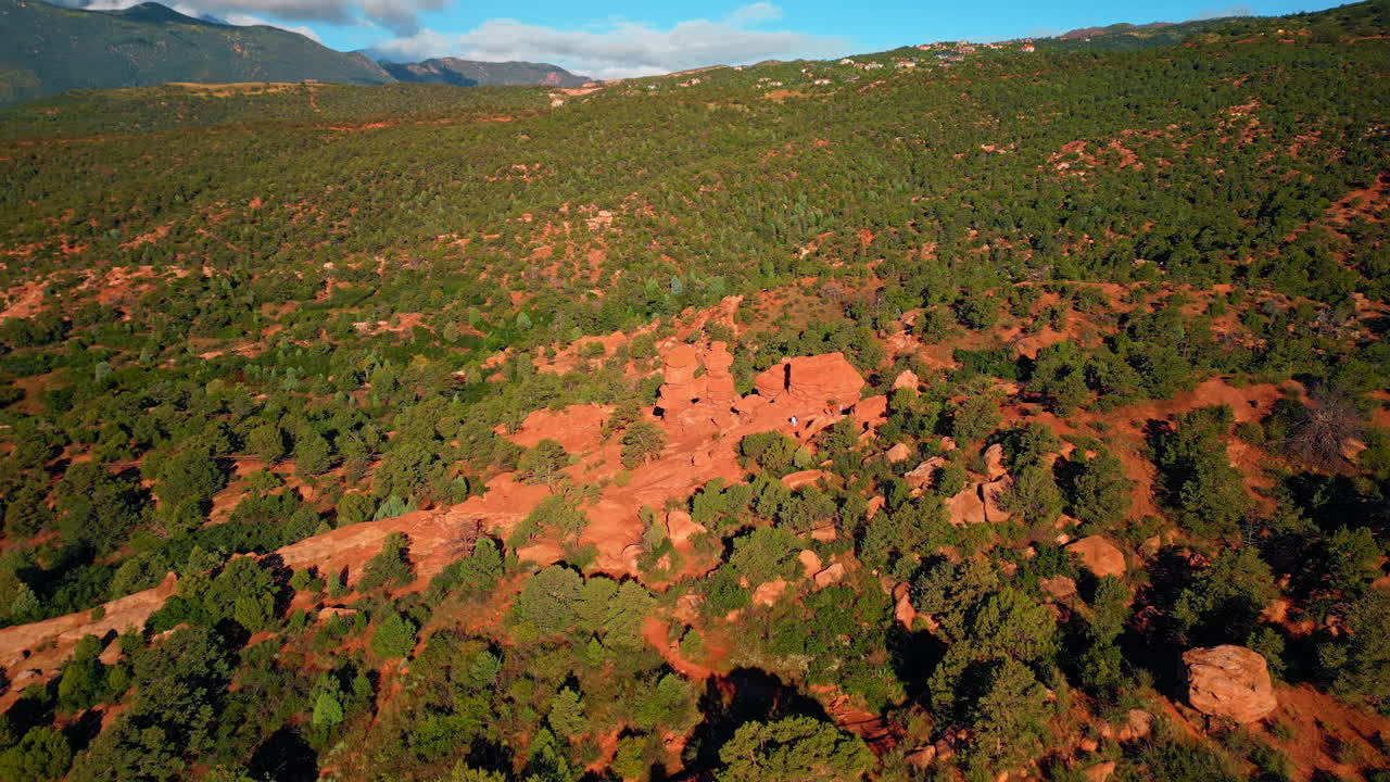 Flight high over the red rocky landscape with whimsical shapes of rocks. Two people take pictures standing on the boulders. Garden of the Gods Park, Colorado Springs, Colorado, USA
