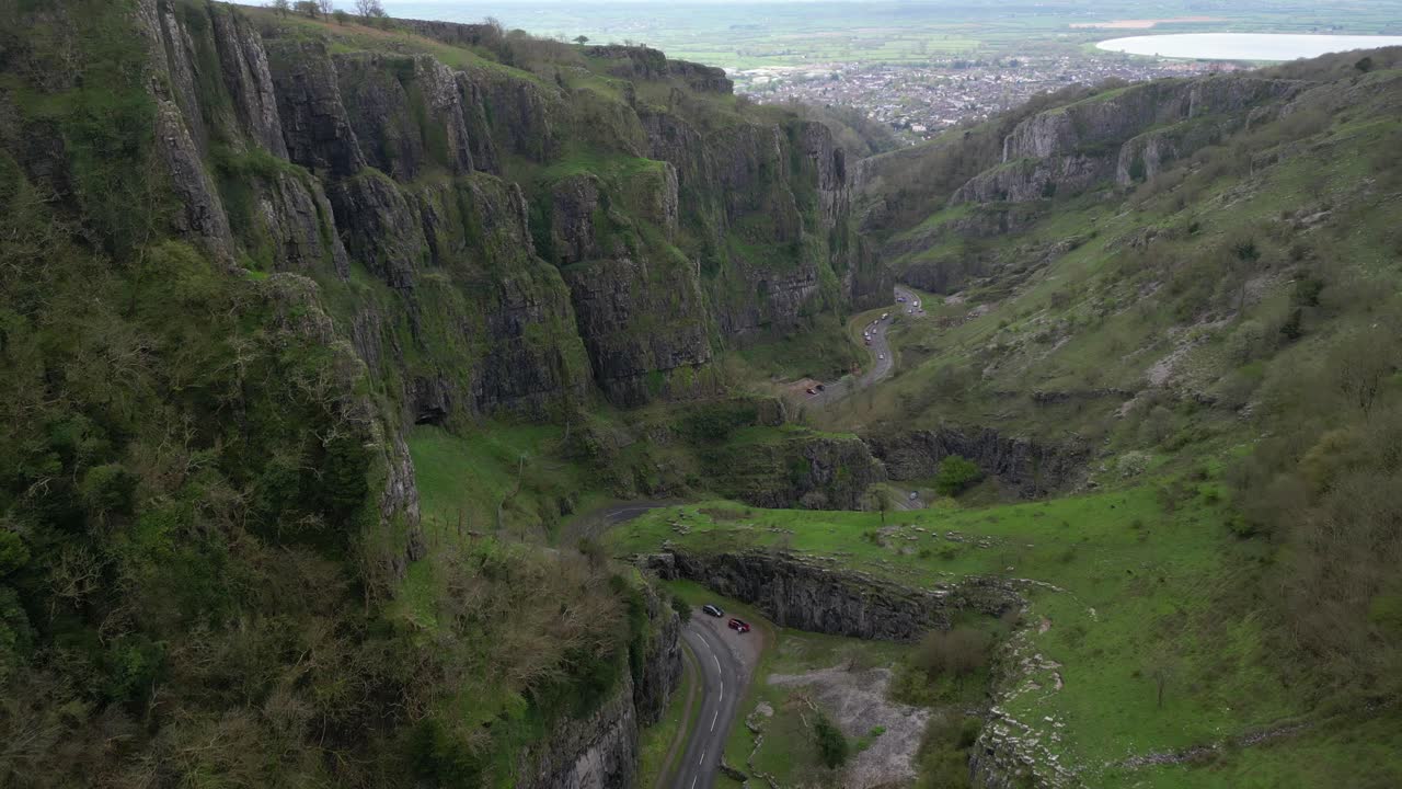 Drone dolly backward over Cheddar Gorge, revealing cliffs, road, and countryside.