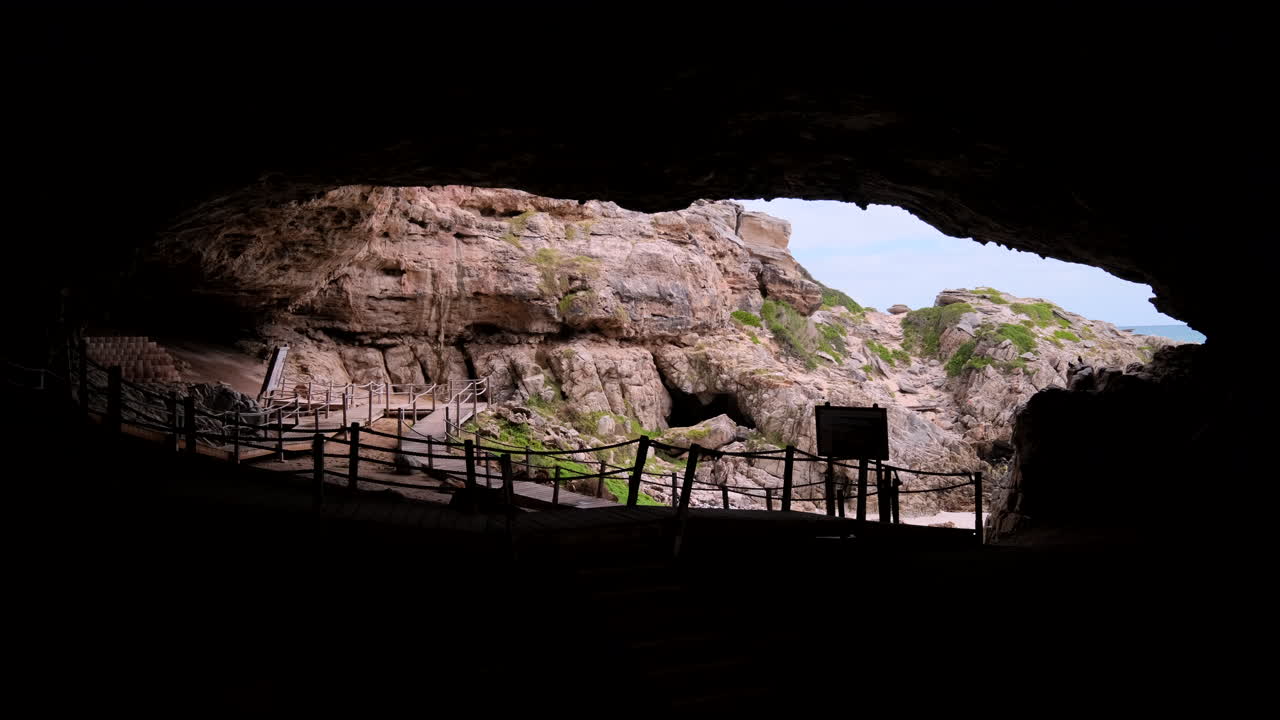 View from dark interior of Klipgat Cave over boardwalk toward rocky exterior