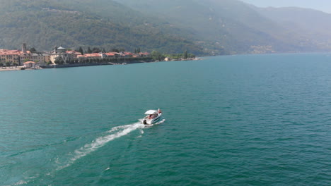 aerial view of a boat cruising on lake maggiore with the beautiful city of cannobio in the background, italy