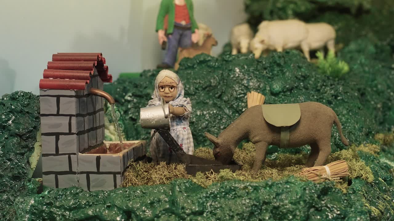 배경 에 양 들 이 있는 당나귀 를 위해 물 을 부는 여자 를 특징 으로 하는 자동화 된 탄생 장면