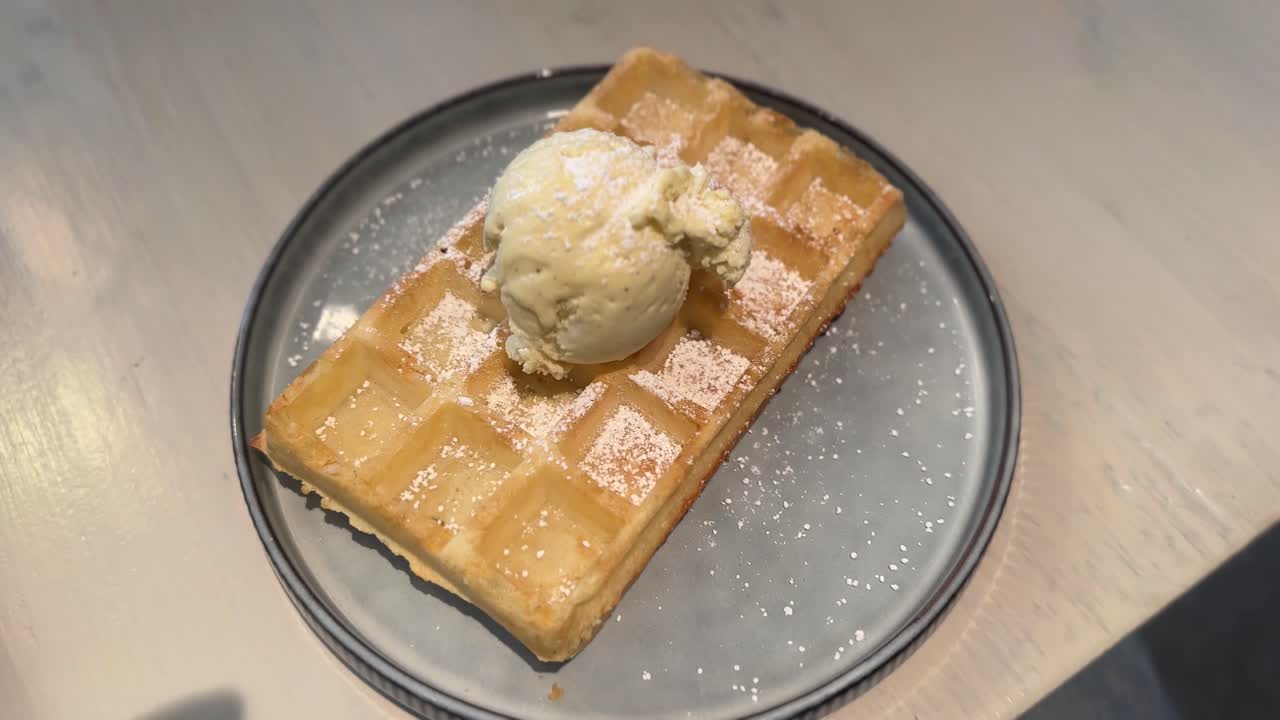 Close-up of a golden Belgian waffle served with a scoop of vanilla ice cream and powdered sugar on a plate