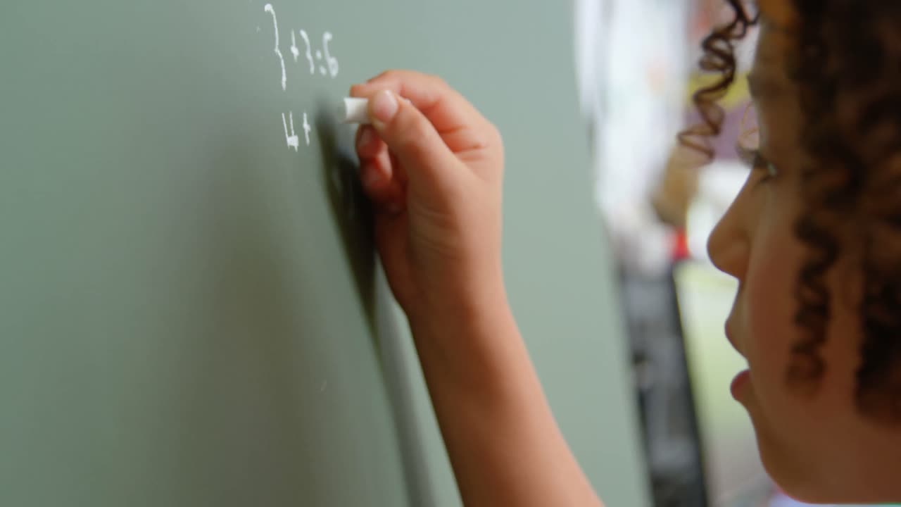Side view of mixed-race schoolgirl solving math problem on chalkboard in classroom at school 4k
