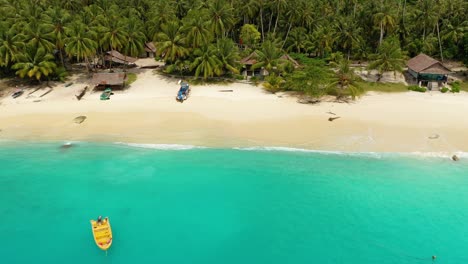 drone volando lejos de la playa con bote y cabañas simples en una isla tropical rodeada de increíbles aguas turquesas en el norte de sumatra, indonesia