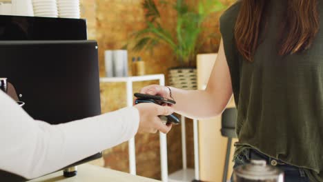 camarera caucásica recibiendo un pago sin contacto y dando una taza de café a una cliente caucásica