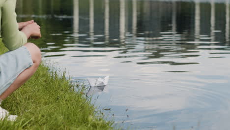 child playing with a paper boat on a lake