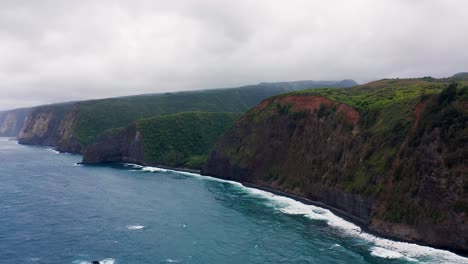 steep rugged cliffs blanketed in lush green vegetation meet rolling blue ocean waves under a heavy overcast sky, creating a dramatic remote coastline filled with wild natural beauty.