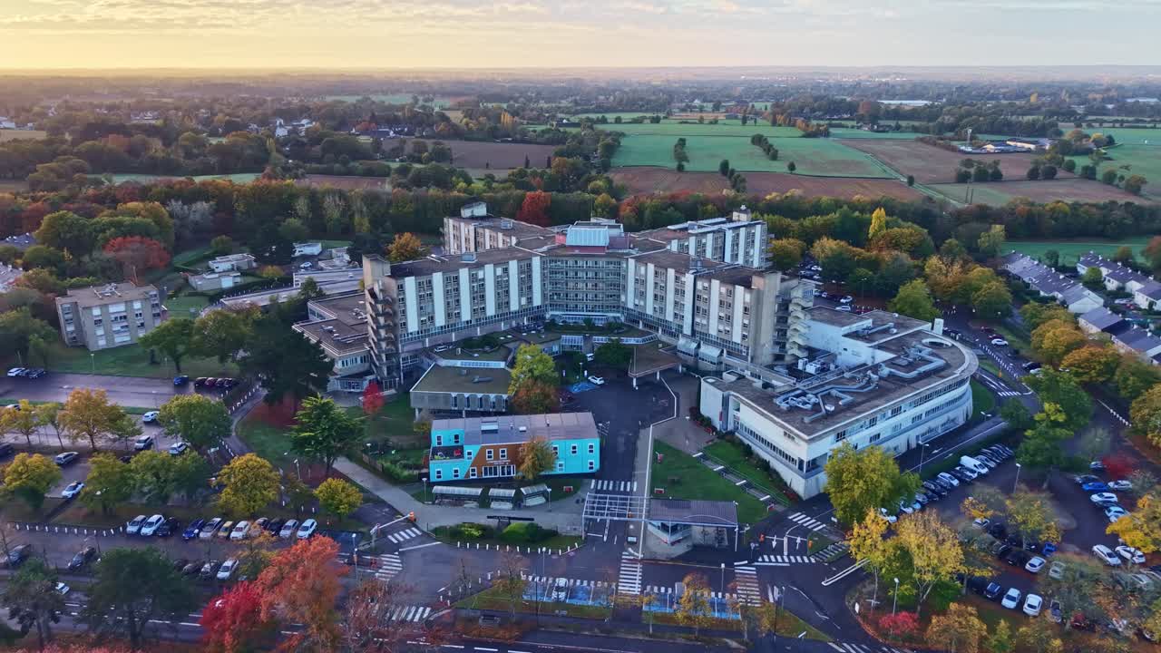 Drone shot at sunrise over Rennes Hospital showing the main building, Women’s House in front, parking lots, nearby houses and surrounding fields