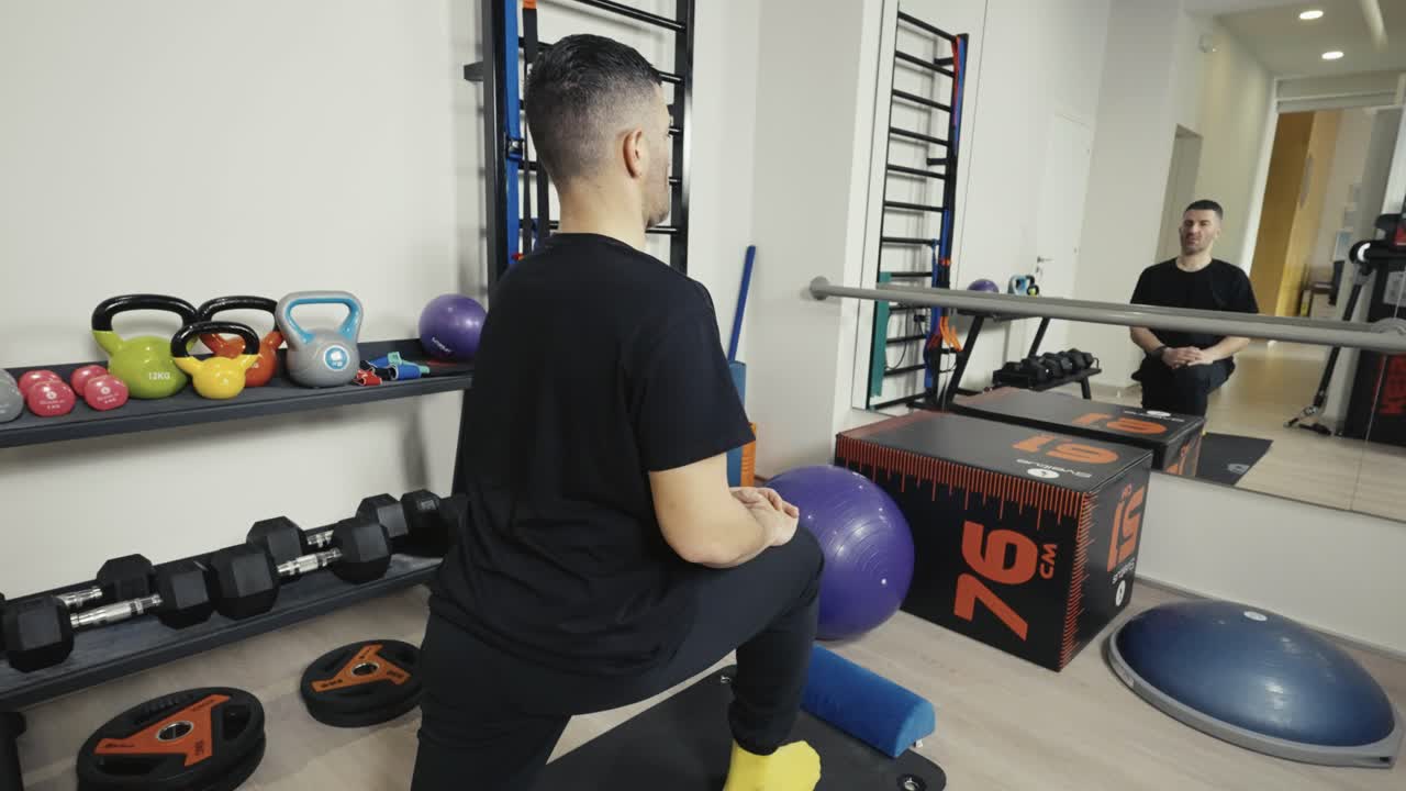 An athletic man doing lunges to stretch his legs while watching himself in the mirror at the gym