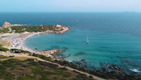 Beautiful-Sardinia-clear-blue-turquoise-and-calm-water-at-a-natural-sand-beach-coast-bay-in-Italy-with-sun-and-sailing-ship