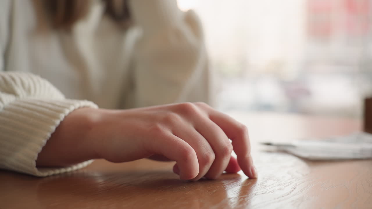 Close up fair skin hand gently tapping wooden table in slow rhythm with soft natural lighting and blurred indoor background creating calm serene atmosphere suggestive of waiting thinking