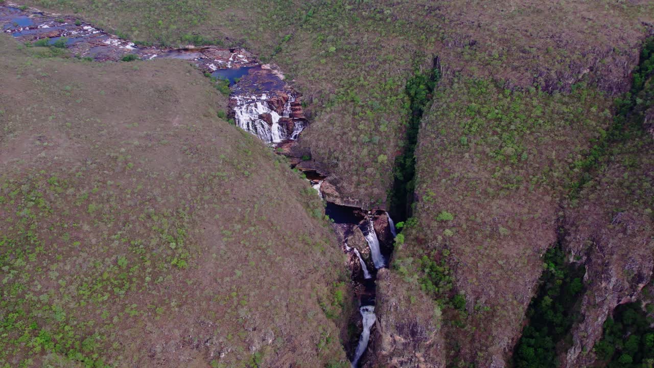 vista aérea capturando la cascada de catarata dos couros que cae en cascada por acantilados rocosos en un exuberante cañón verde en el parque nacional de chapada dos veadeiros, revelando la belleza cruda de la naturaleza, movimiento lento ángulo bajo