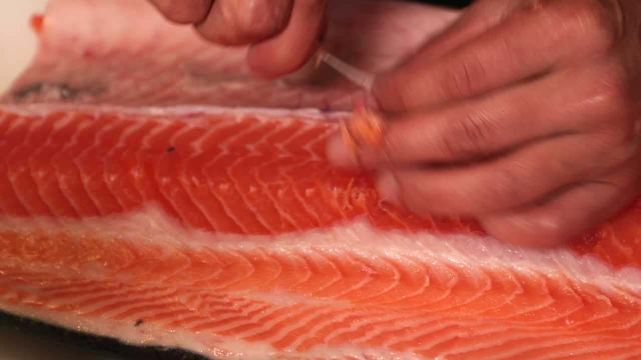 manos de persona quitando espinas de una carne de salmón cruda
