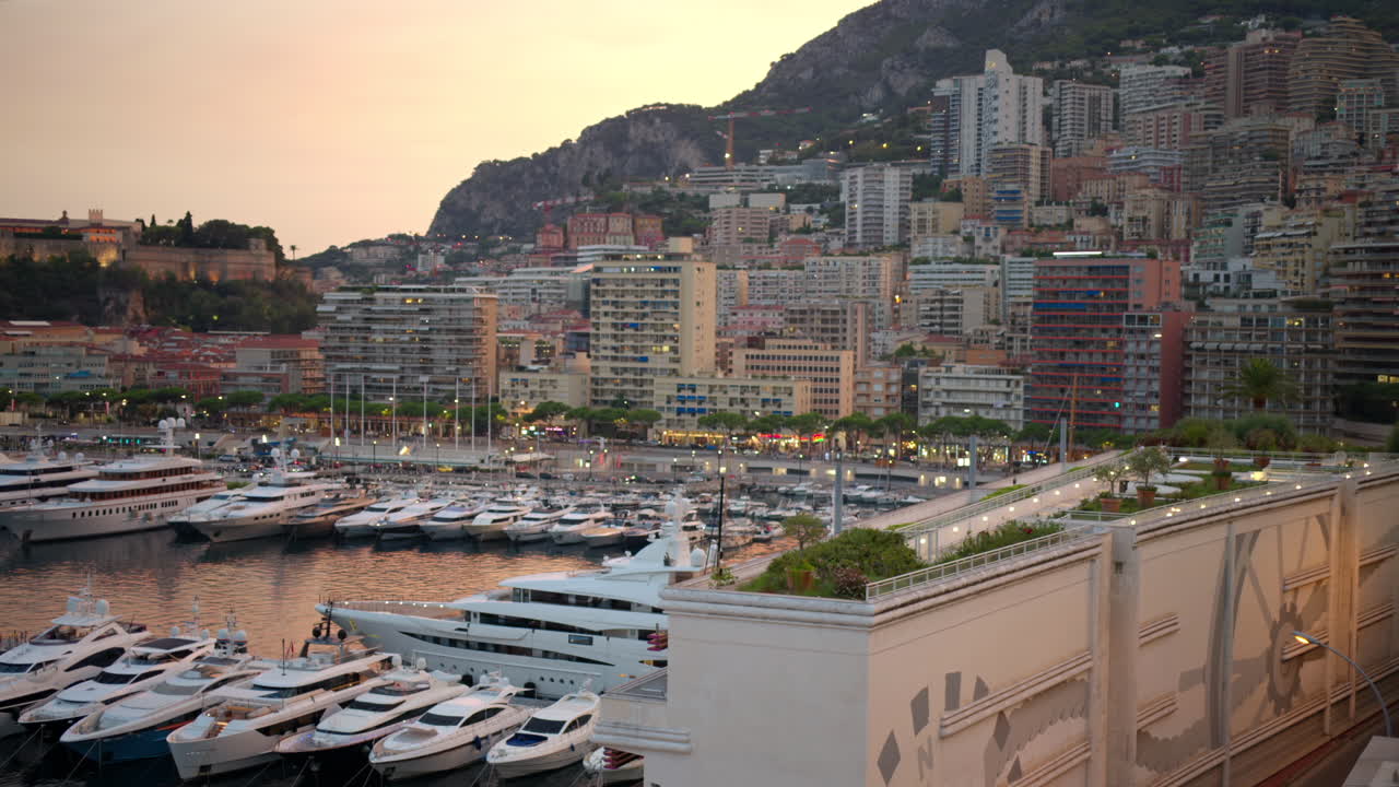 Cityscape of Monaco at sunset. Sea port with moored yachts, residential buildings and streets with illumination