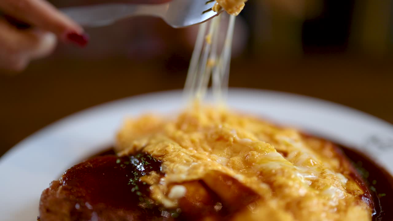 Close-up of fork lifting gooey cheese from omurice with demi-glace, soft natural lighting