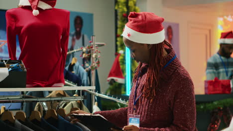 portrait of cheerful manager browsing through festive clothing display in christmas shopping store, making sure clothes are ready for customers during winter holiday bargains season