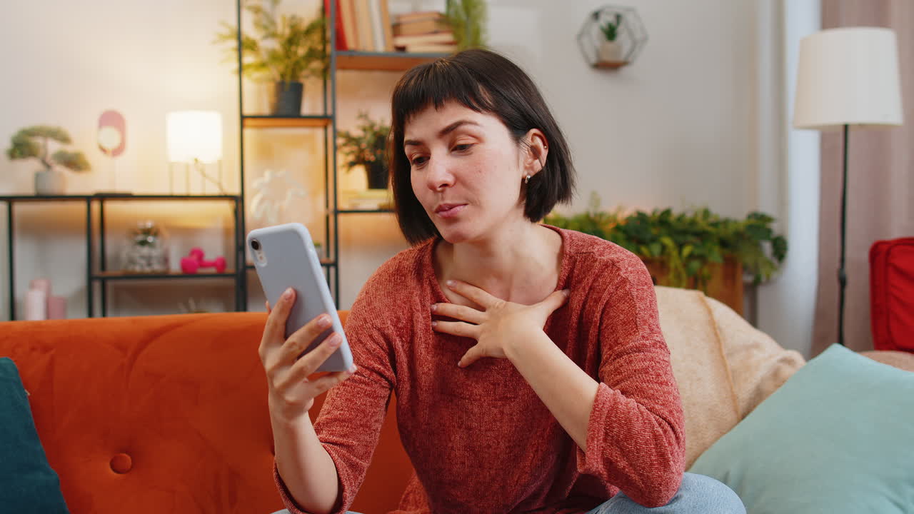 mujer joven sonriente teniendo una conversación con un amigo en un teléfono móvil sentada en el sofá en casa