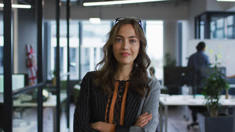 portrait of caucasian businesswoman standing in office with arms crossed smiling to camera