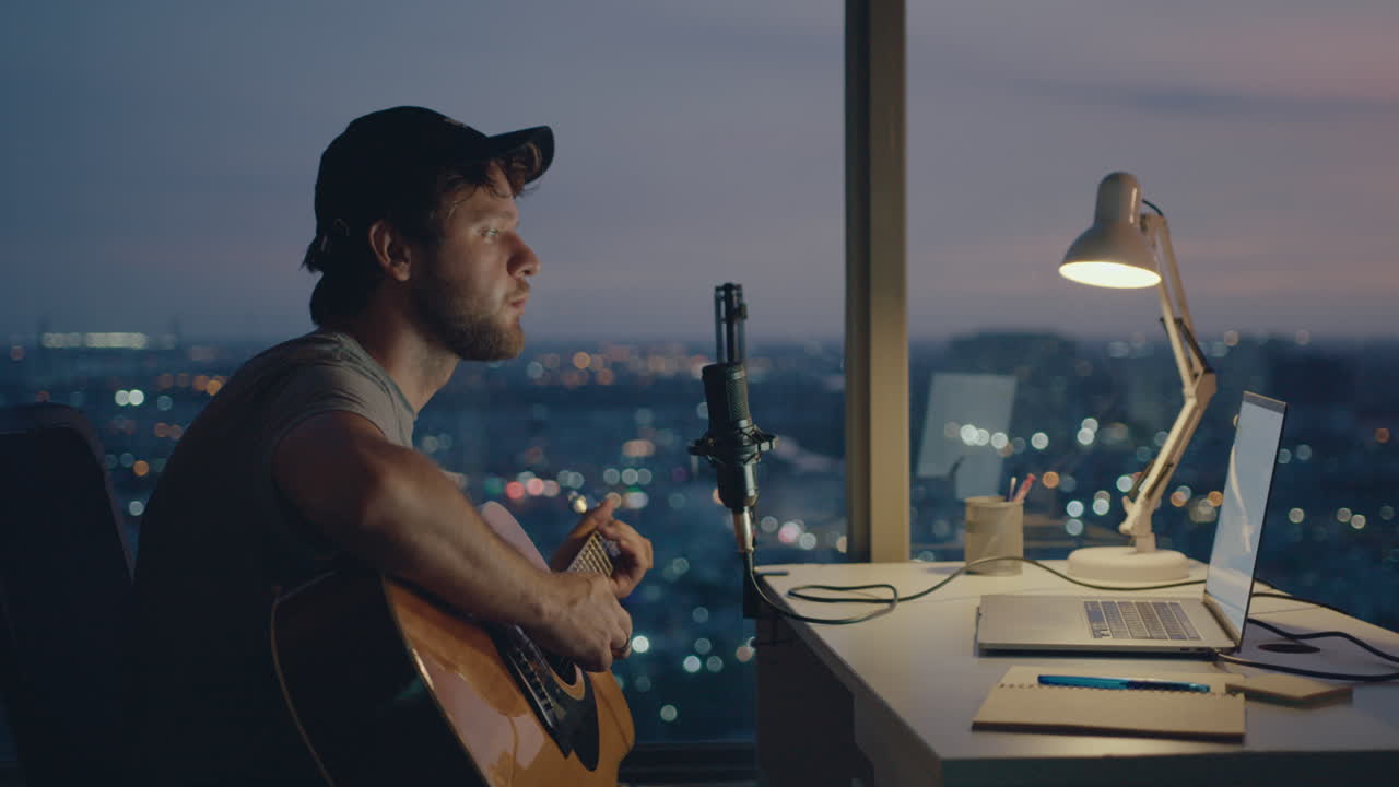 En skægget mand indspiller en sang med en guitar med panoramaudsigt over byen