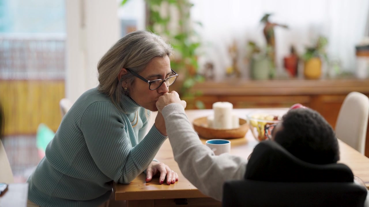 Mature Woman Holding Hands with Person in Wheelchair at Home
