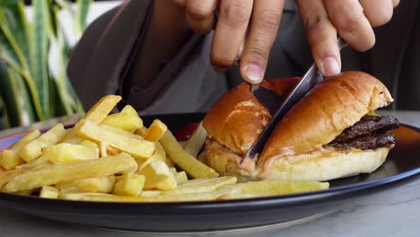 un primer plano de una persona comiendo una hamburguesa con queso y papas fritas