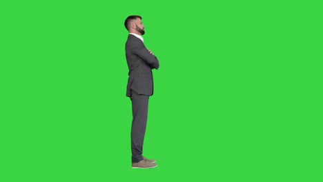 confident business man with beard and mustashes in suit standing with folded hands on a green screen, chroma key