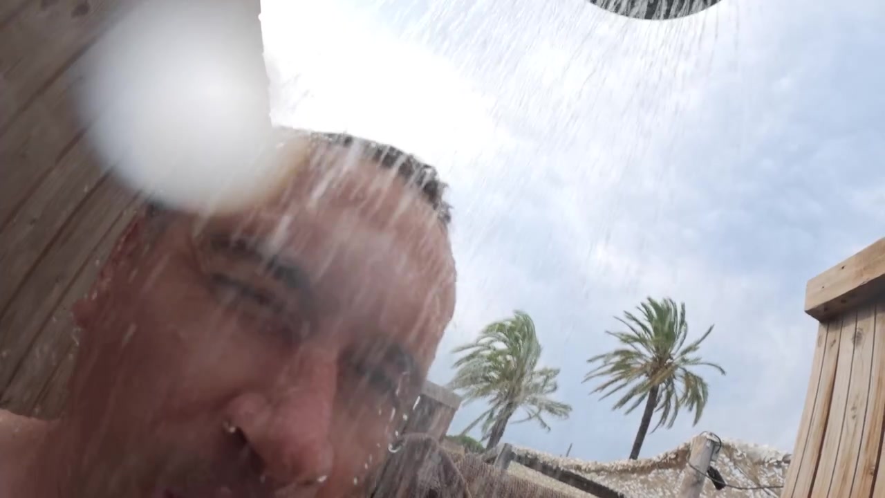 Hombre lavándose la cabeza y el cabello bajo el agua corriente en una ducha exterior rústica de madera, sintiéndose limpio y vigorizado.