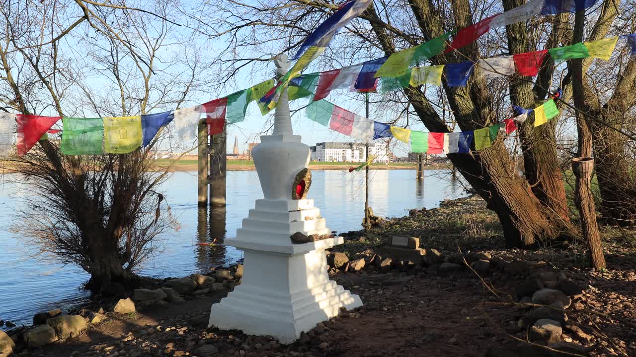 바람에 날리는 형형색색의 기도 깃발과 함께 나무와 초목으로 둘러싸인 주트펜(zutphen)의 ijssel 강 가장자리에 있는 작은 불교 사리탑 장식의 친밀한 장면