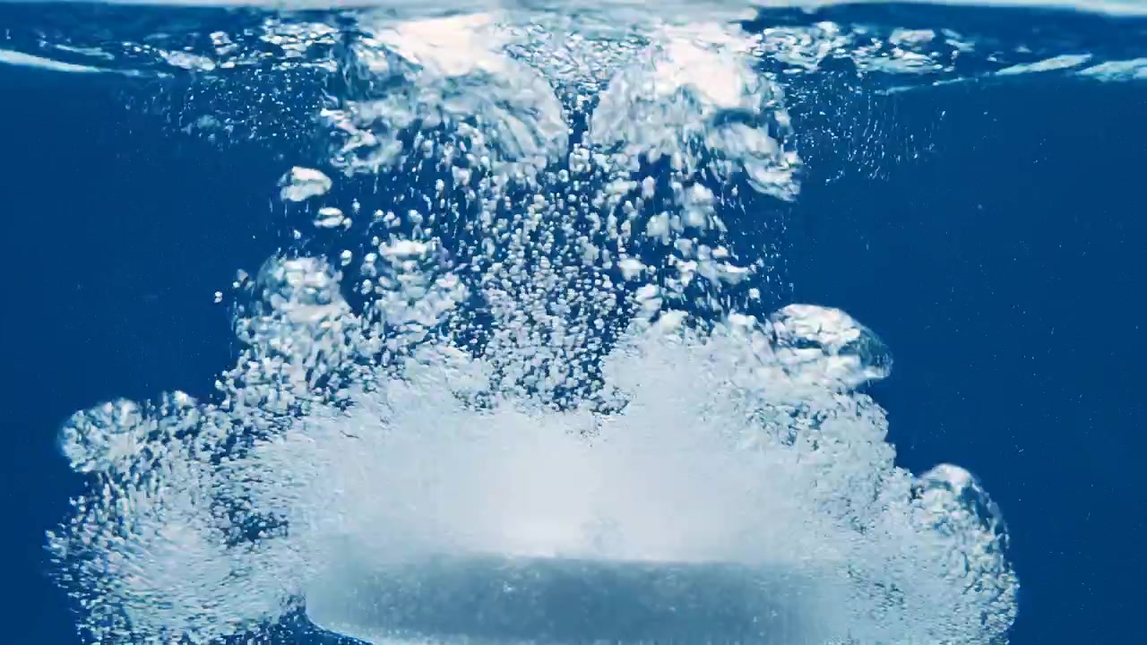 Compressa bianca effervescente che si dissolve in acqua blu con bollicine