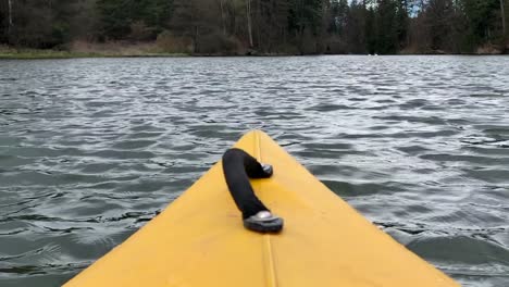 a yellow color nose of kayak moving along in forest calm river on a nice sunny day, outdoor activities