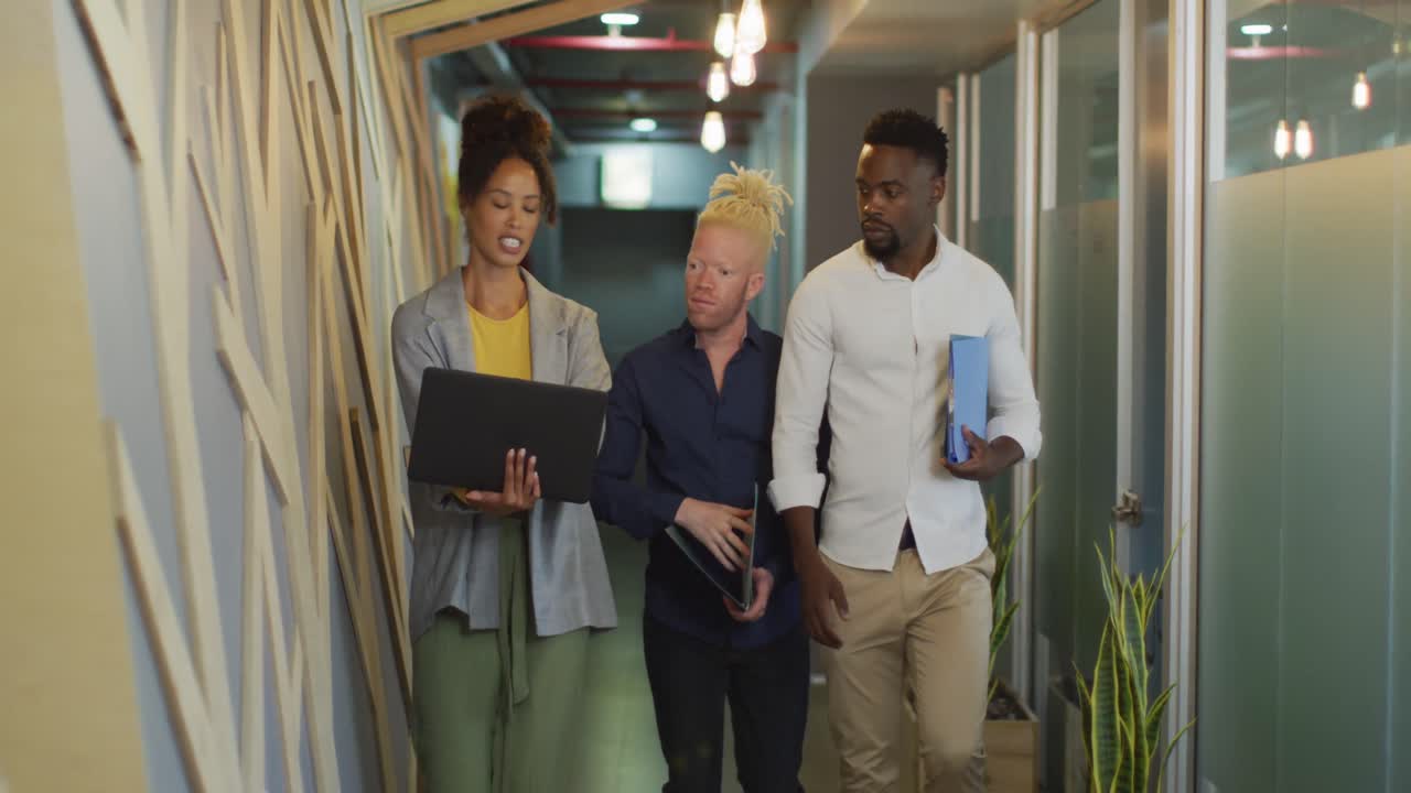 Diverse business people discussing with laptop and walking in creative office