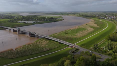 drone flying backward over the jann berghaus bascule bridge near leer, showing the ems river, levees, roads, and surrounding countryside under dramatic spring skies.