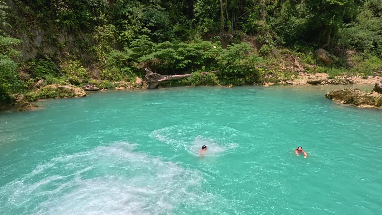 Un uomo si lancia nell'acqua azzurra brillante mentre fa canyoning alle cascate Kawasan a Cebu, Filippine.