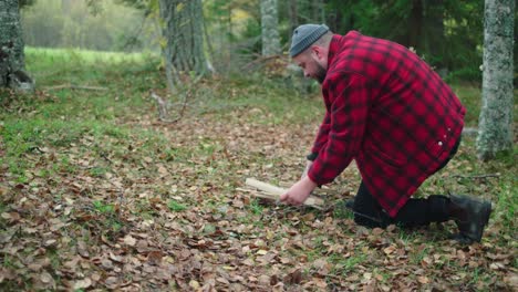 man trying to light a fire with logs in the middle of the forest