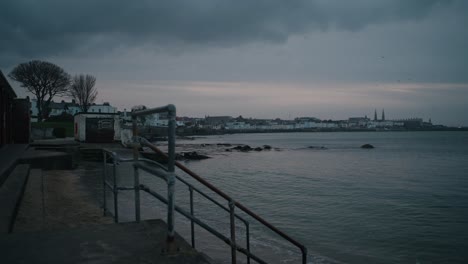 a moody evening view from sandycove beach overlooking dublin bay and dun laoghaire. dark clouds fill the sky as gentle waves lap against the shore.