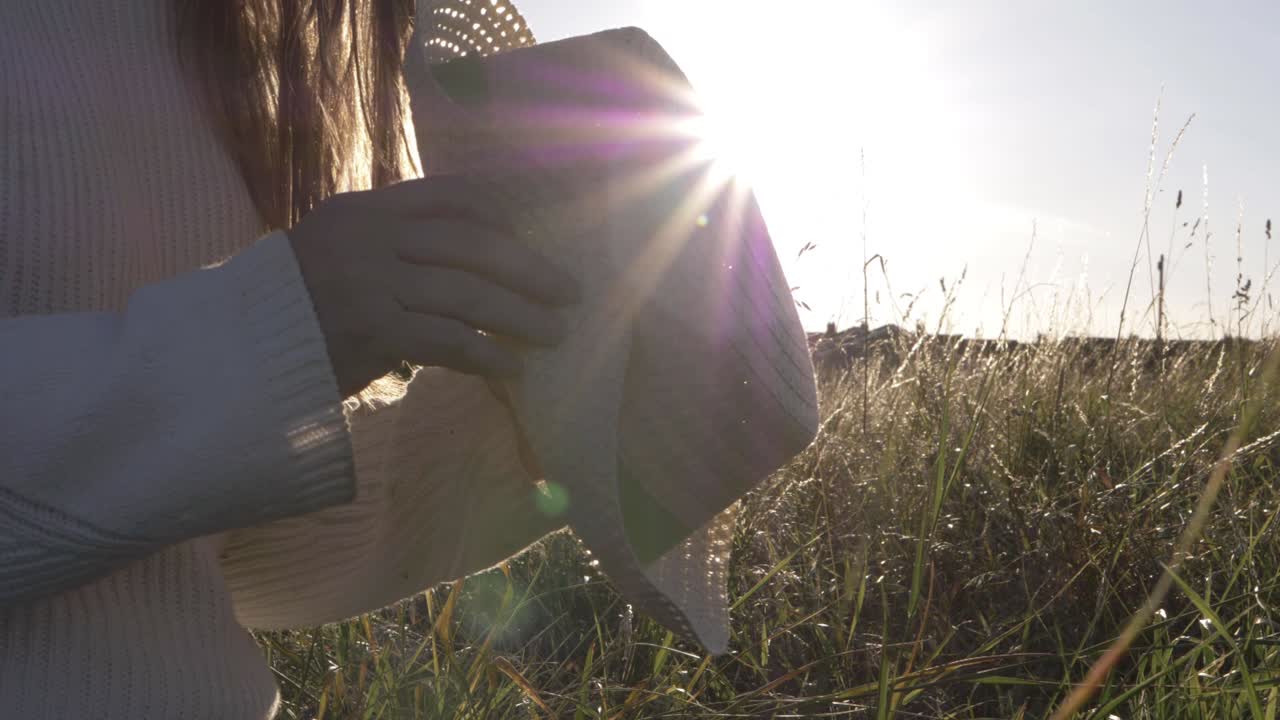 Woman holding straw hat in summer background at dusk medium shot