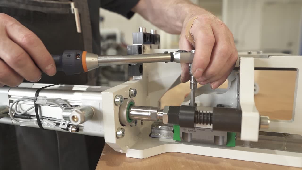 Technician adjusts and tightens the lead screw drive of a precision linear module. Close up of mechanical fine tuning during industrial assembly