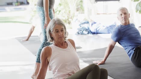 Group-of-diverse-seniors-practicing-pilates-with-female-coach-in-sunny-room,-unaltered,-slow-motion