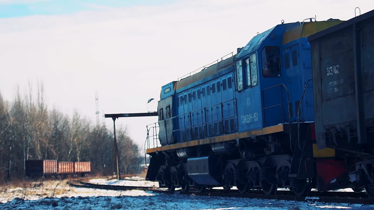 Una locomotora diésel arrastra vagones con carga en una estación de ferrocarril nevada.