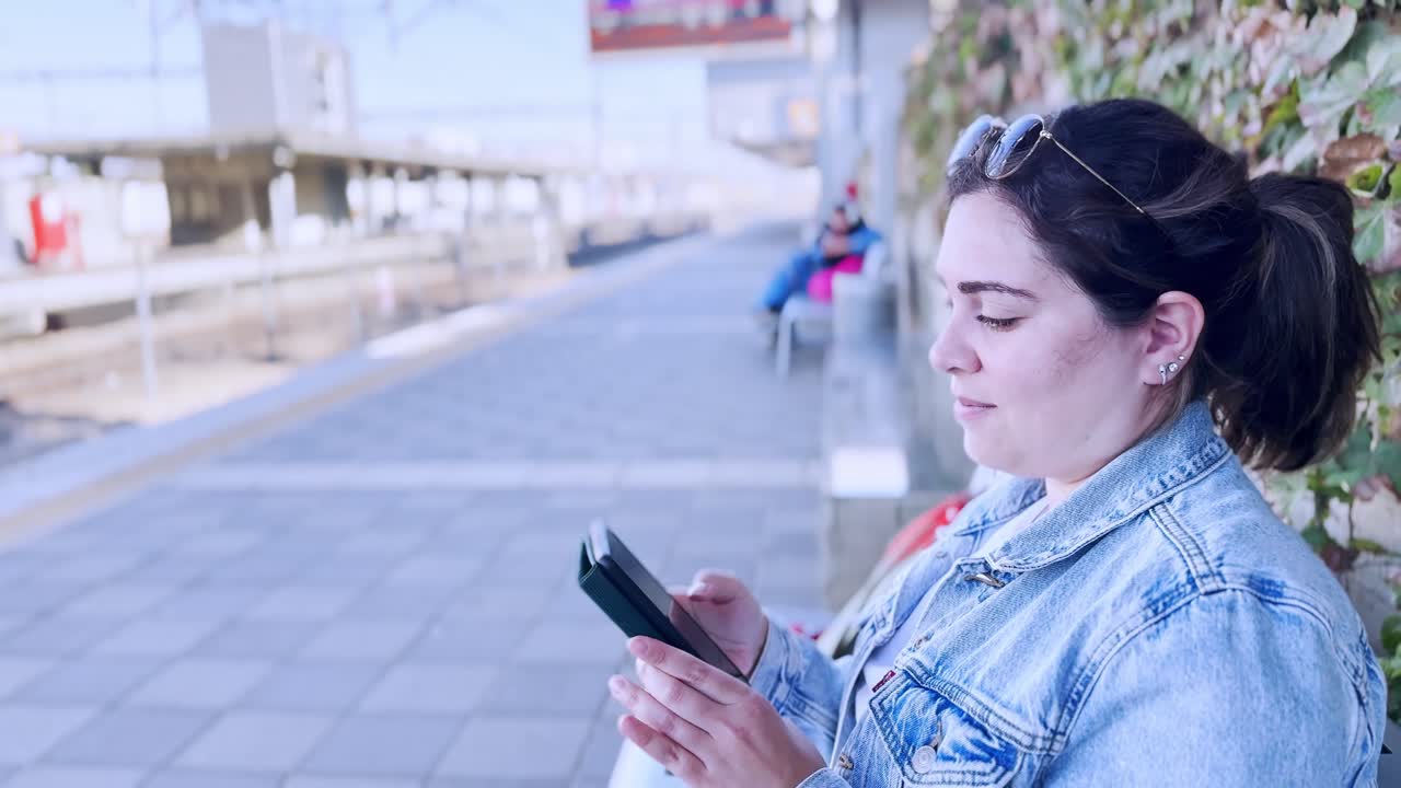 Young Woman Holding and Looking at Her Smartphone Screen at a train station platform
