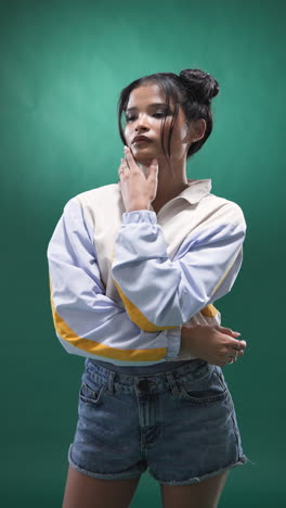 vertical video: young woman in stylish jacket adjusting hair, posing confidently in studio